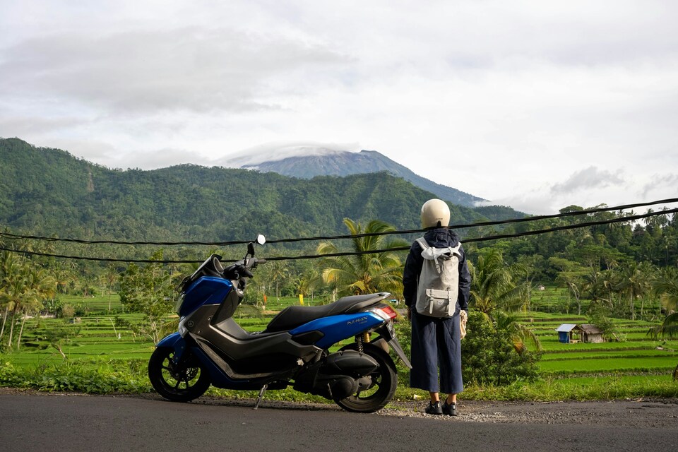 A scooter and a female standing on the right side looking far ahead