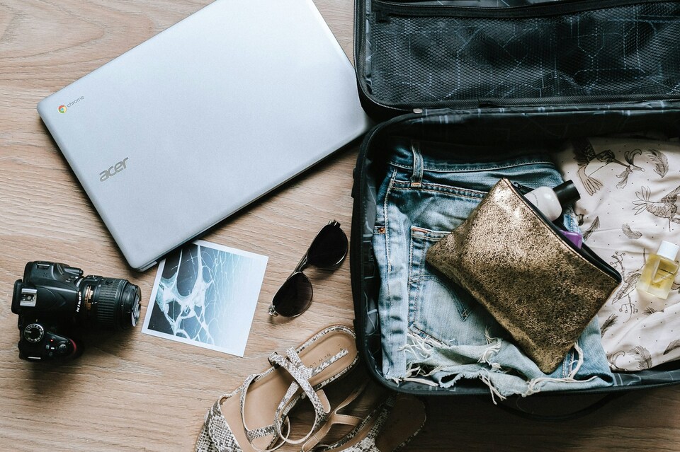 A laptop, camera, glasses, shoes, photo and a travel bag with cloths and a purse in it